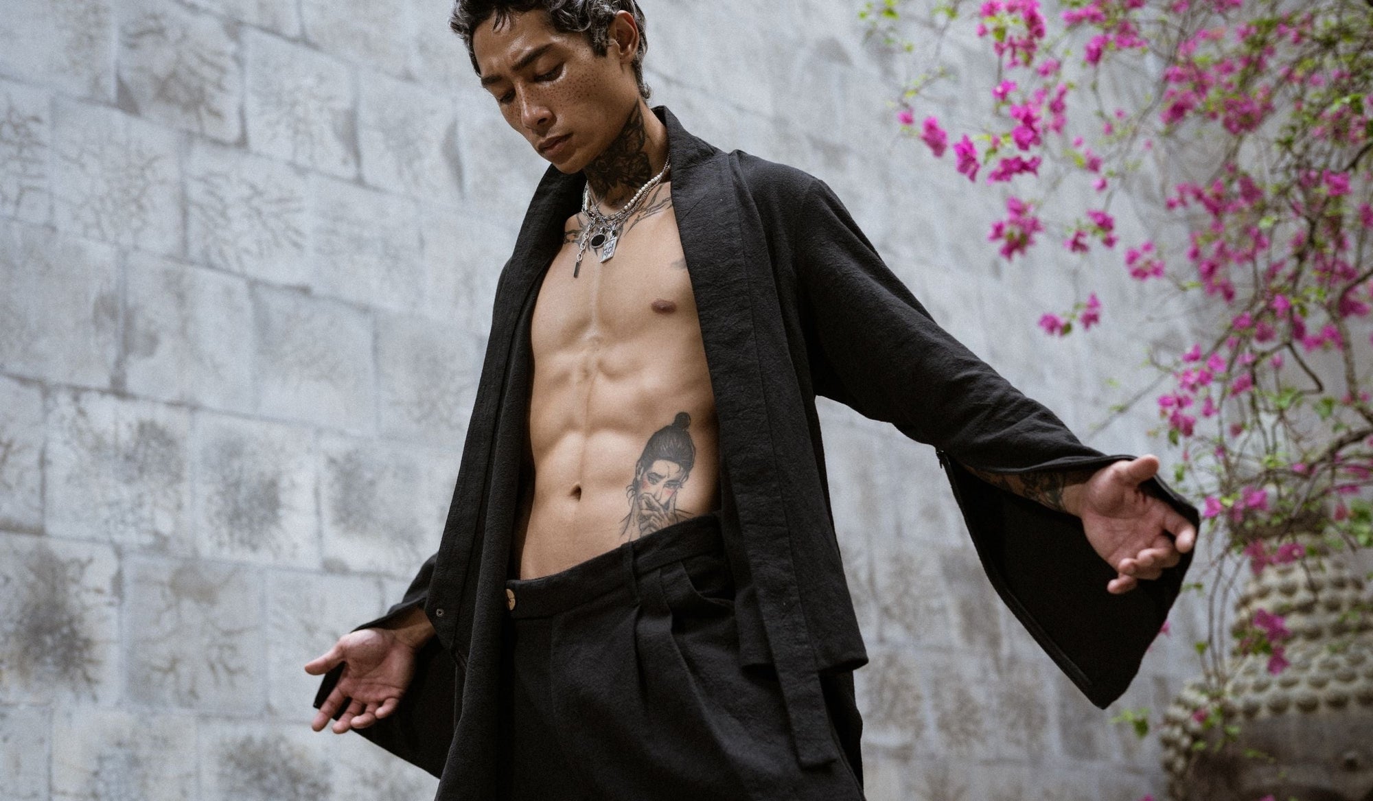 Man standing still in flowing black kimono, arms open, centered posture — controlled presence and inner discipline