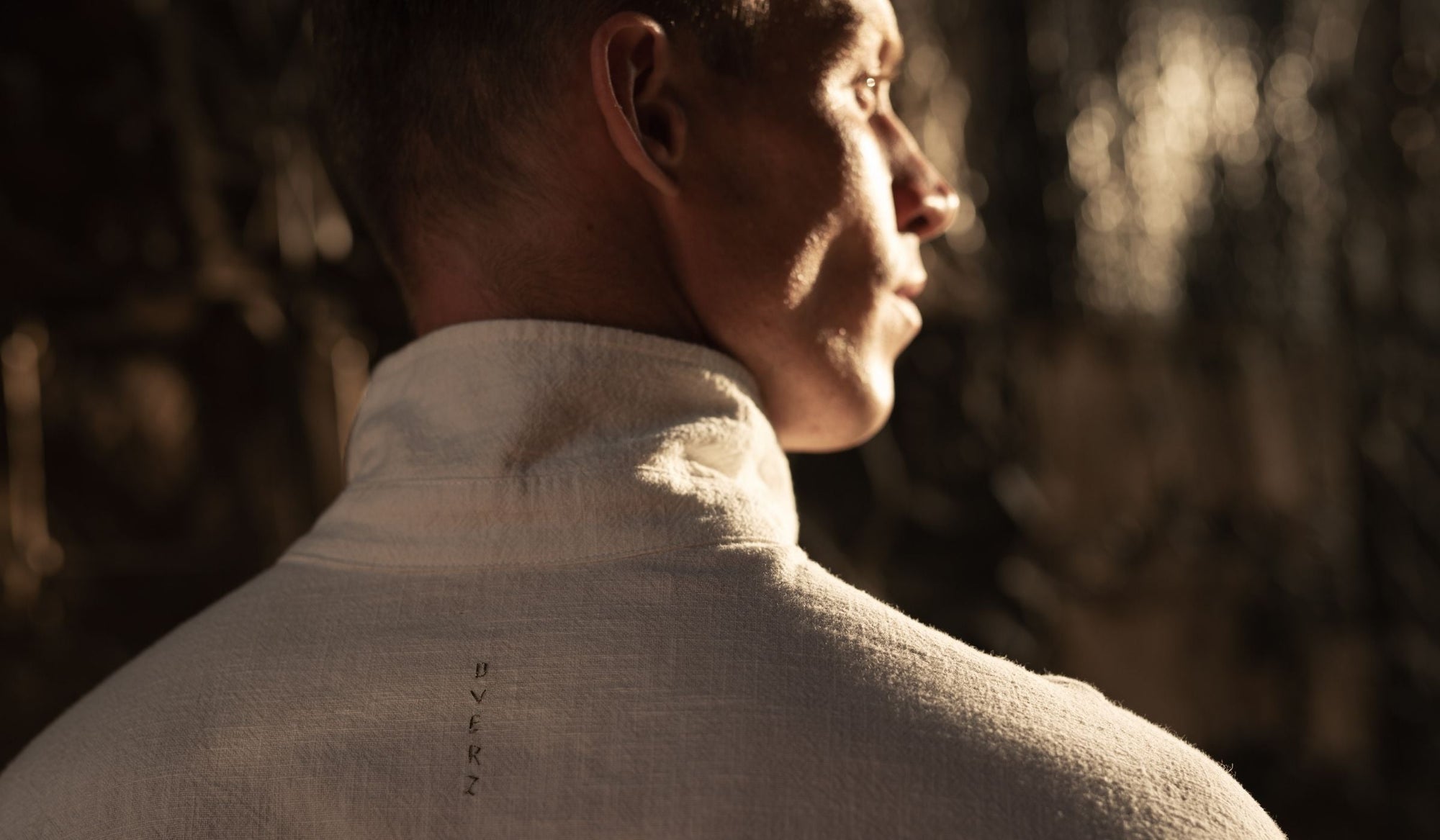 Close-up of a man’s back and neck in structured white garment, standing upright in warm light, emphasizing posture and alignment