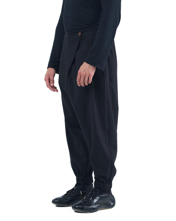 Black asymmetric jogger pants with elastic cuffs and textured fabric by OVERZ