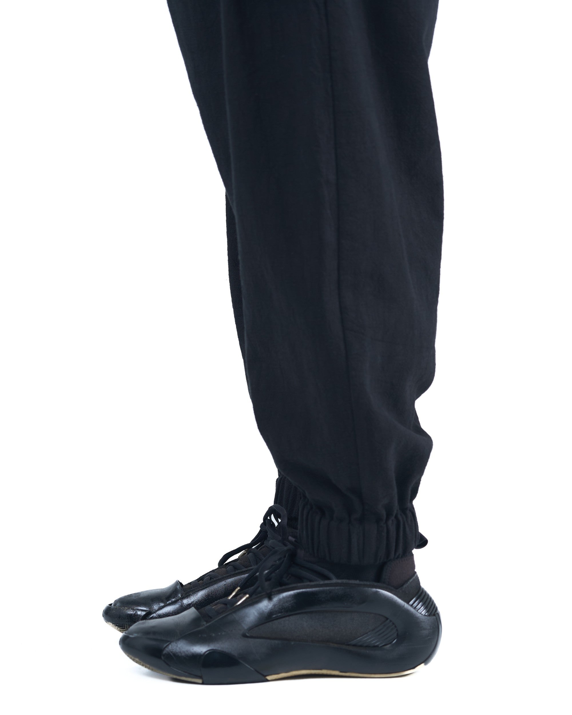 Black asymmetric jogger pants with elastic cuffs and textured fabric by OVERZ