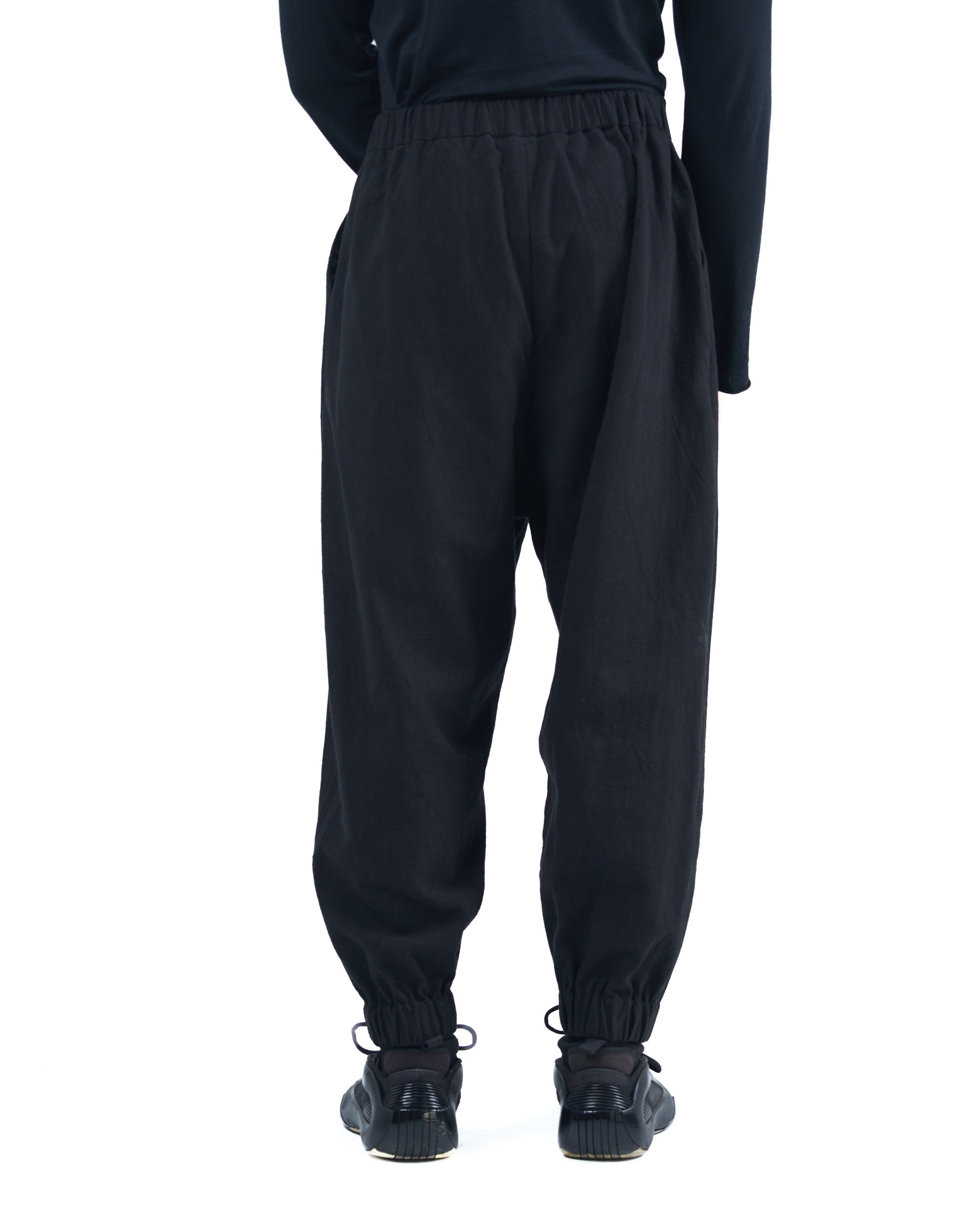 Black asymmetric jogger pants with elastic cuffs and textured fabric by OVERZ