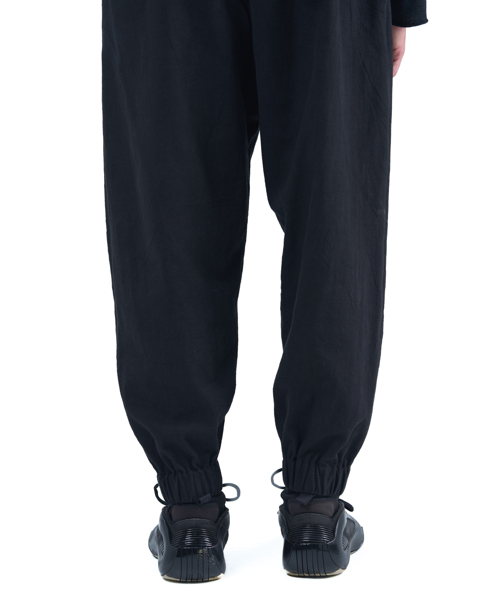 Black asymmetric jogger pants with elastic cuffs and textured fabric by OVERZ
