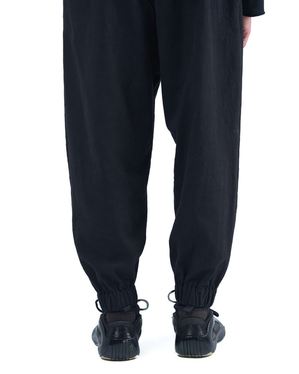 Black asymmetric jogger pants with elastic cuffs and textured fabric by OVERZ